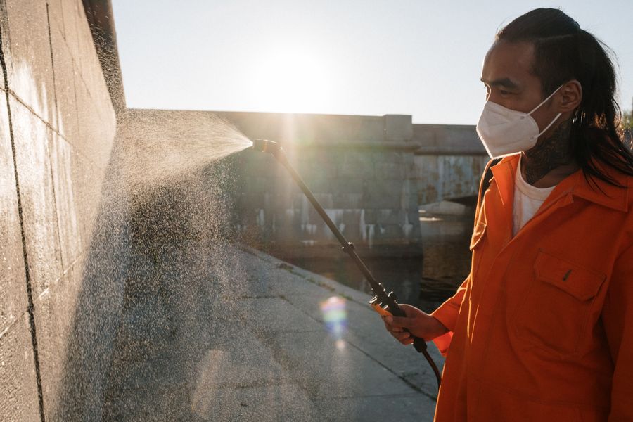 Pest control technician spraying treatment along an exterior wall